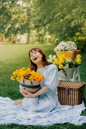 Joyful outdoor portrait with yellow flowers and picnic setup on blue blanket.