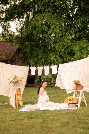 Outdoor maternity scene with white linens, baby clothes, and decorative accents against a rustic barn backdrop.