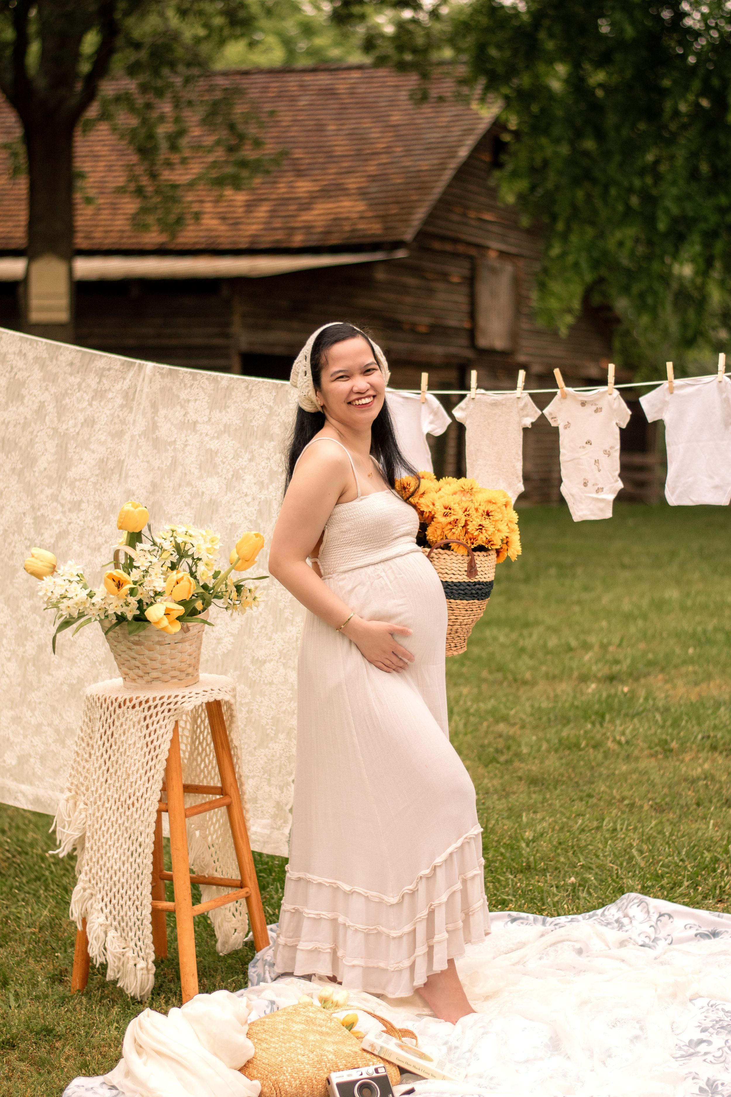 Outdoor maternity portrait with rustic decor, hanging baby clothes and yellow flowers.