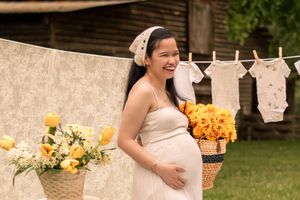Maternity photo featuring white dress, sunflowers and vintage baby clothes display.