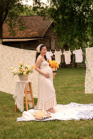 Joyful maternity moment captured in garden setting with vintage baby clothes and decor.