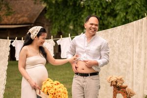 Outdoor maternity photoshoot setup with white lace curtains hanging on a clothesline and rustic wooden stools.