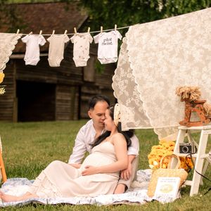Outdoor pregnancy photography setup featuring hanging white linens and decorative elements in a grassy field.