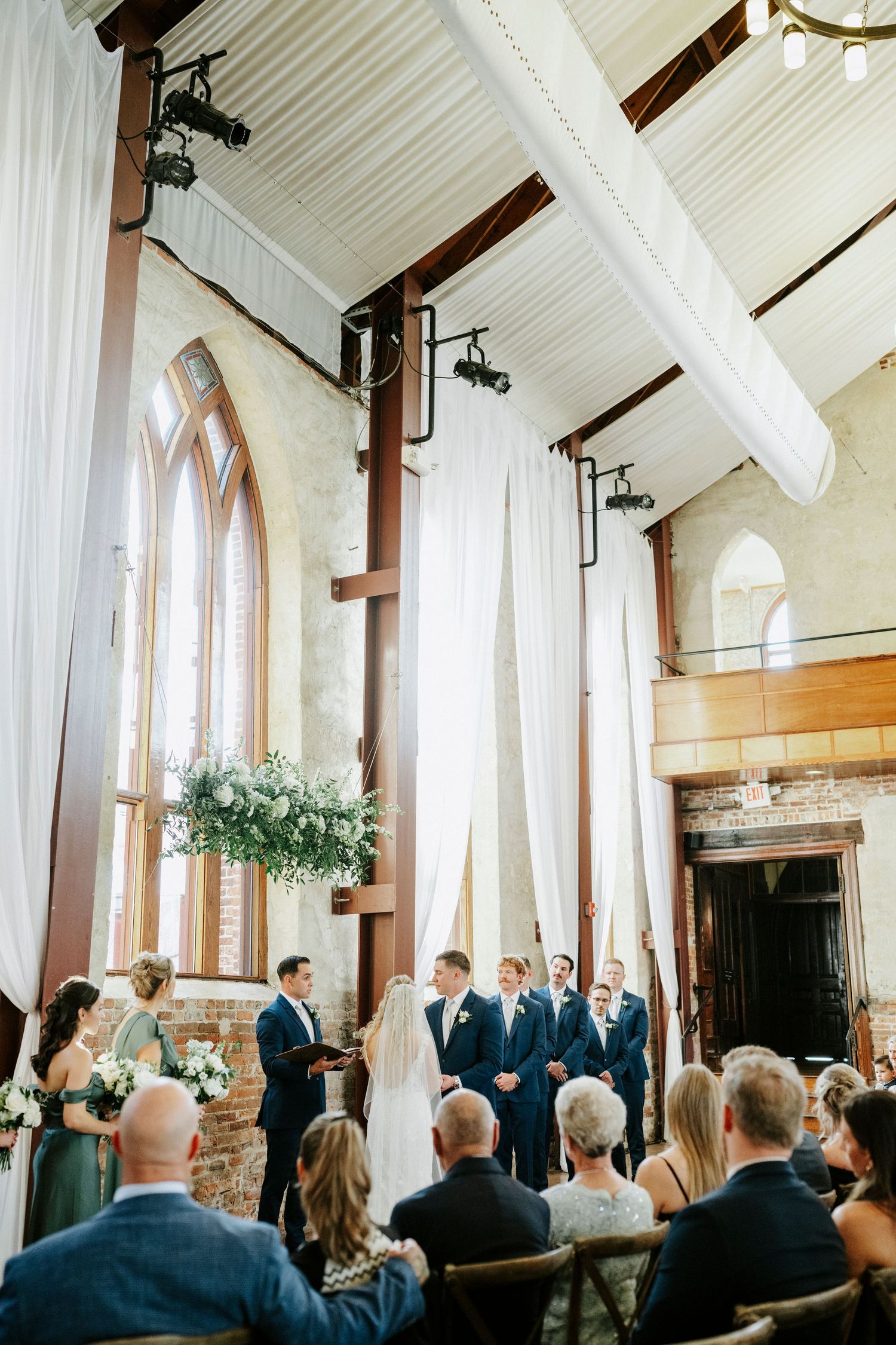 Wedding ceremony taking place in a historic church with vaulted white ceilings and arched windows.