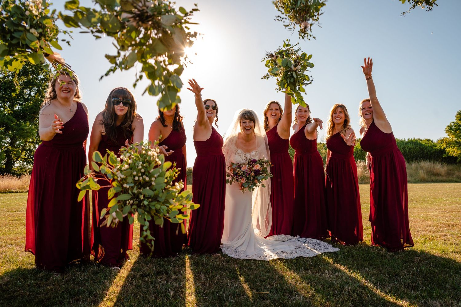 Golden hour photo of a bride and her bridesmaids tossing their bouquets at the camera at Wootton Park, Henley in Arden..