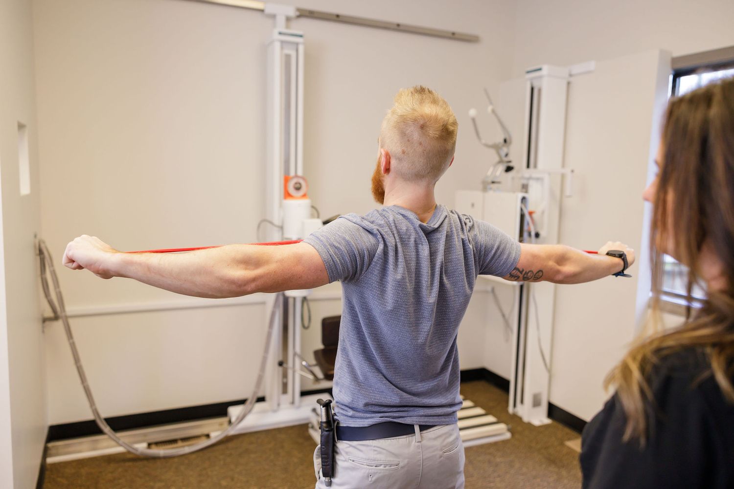 chiropractor branding photo in Sumner, WA wellness health man demoing resistance bands for the upper body arms pectorals woman watching