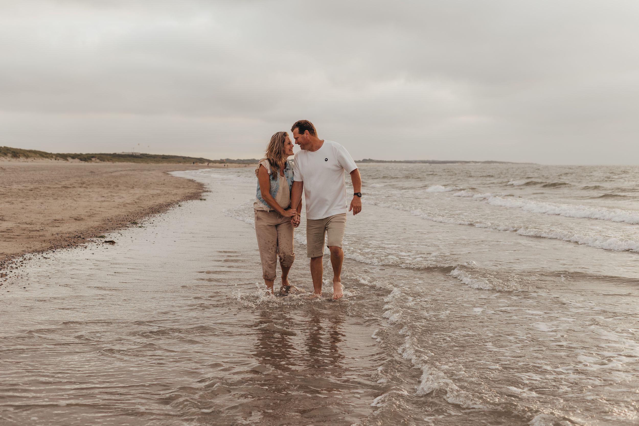 verliefde stel lopen hand in hand door de branding op het strand