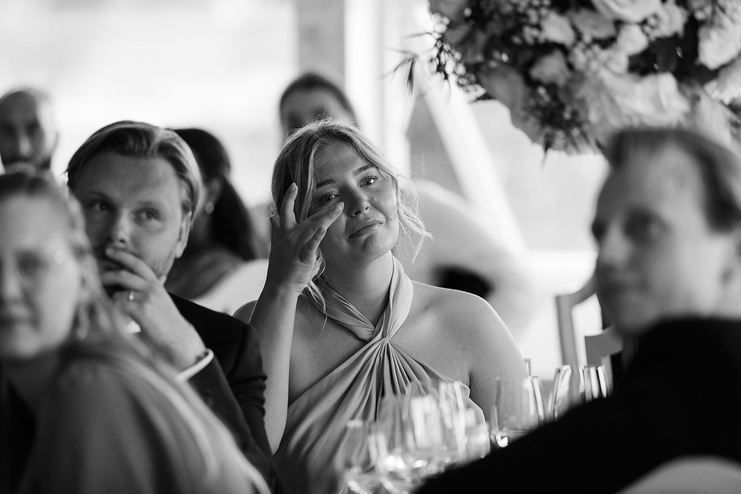 Black and white candid photo of wedding reception guests laughing and enjoying themselves at a formal dinner table.
