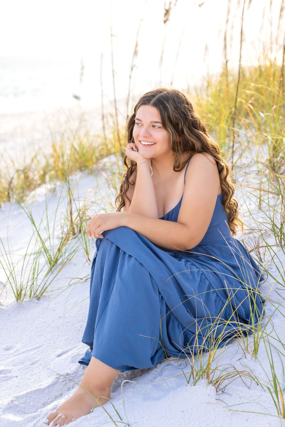 Person in a blue dress relaxing on white sandy beach dunes during golden hour.