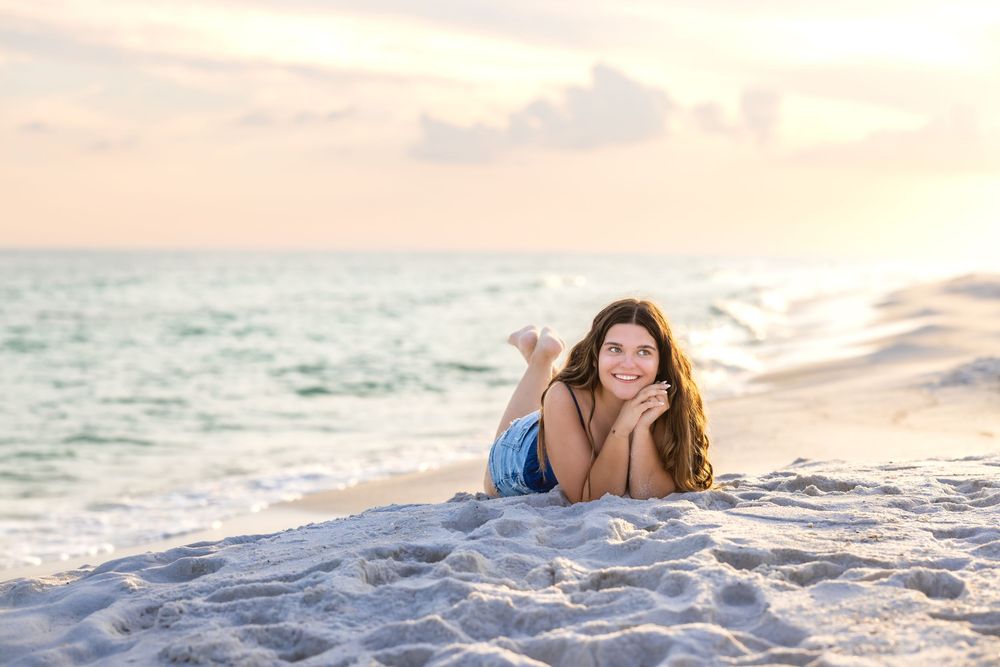 A person in casual attire relaxes on pristine white sand during a beach sunset photoshoot.