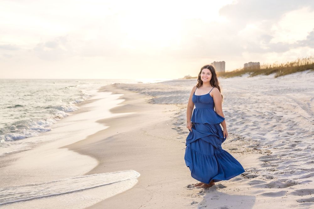 Someone wearing a royal blue dress poses gracefully by the ocean waves during a beach photoshoot.