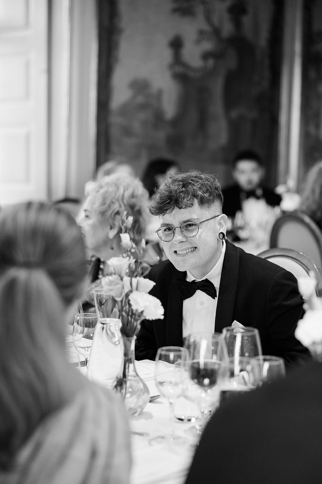 A candid black and white photo of guests smiling and socializing at an elegant dinner reception.