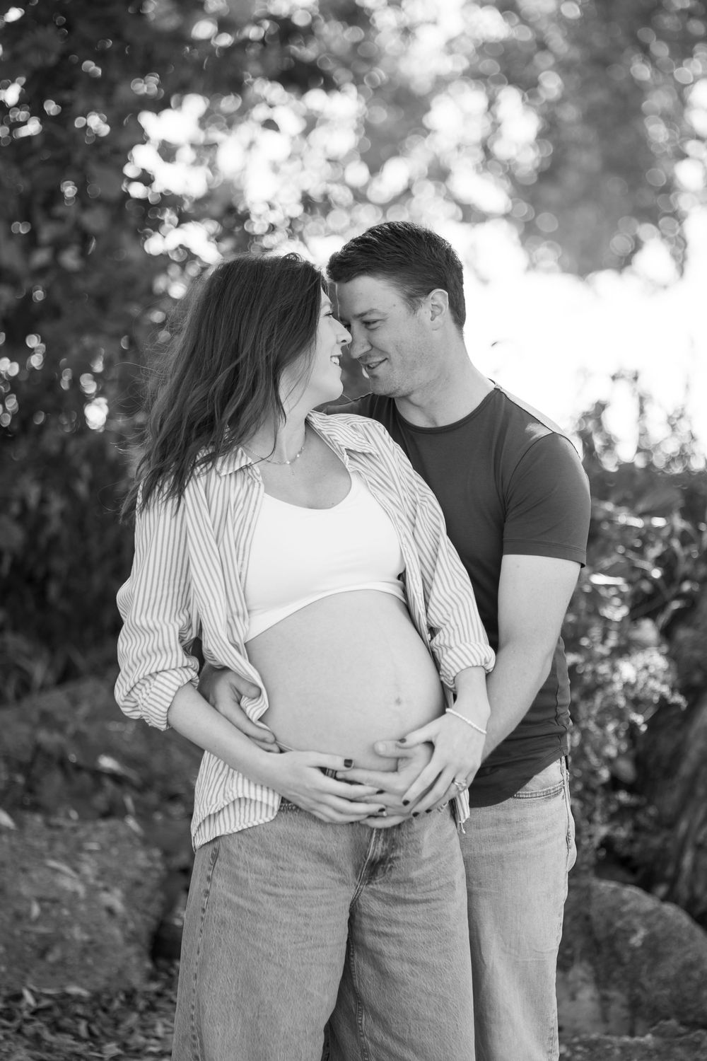 Black and white maternity photo of an expecting couple sharing an intimate moment outdoors.