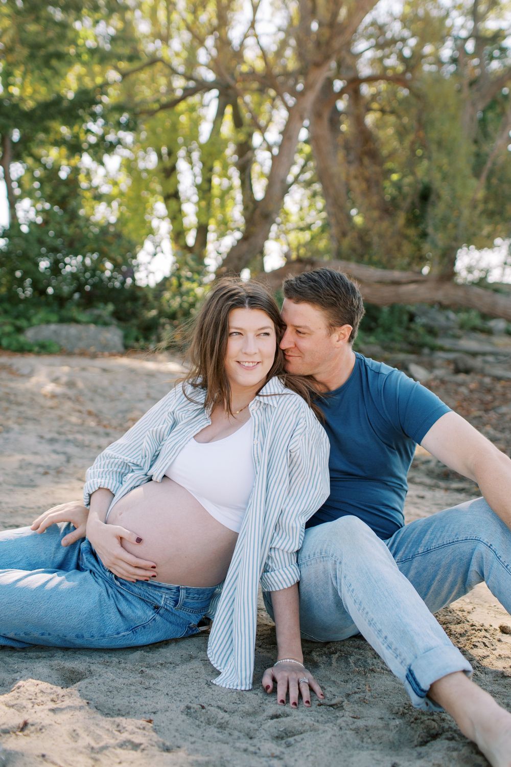 Intimate maternity photo session outdoors with couple relaxing on sandy ground.