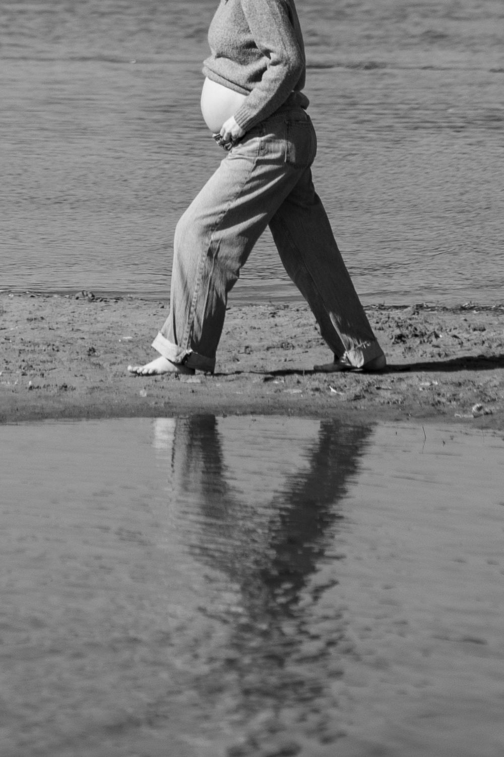Black and white photo of feet walking along the shoreline in shallow water.