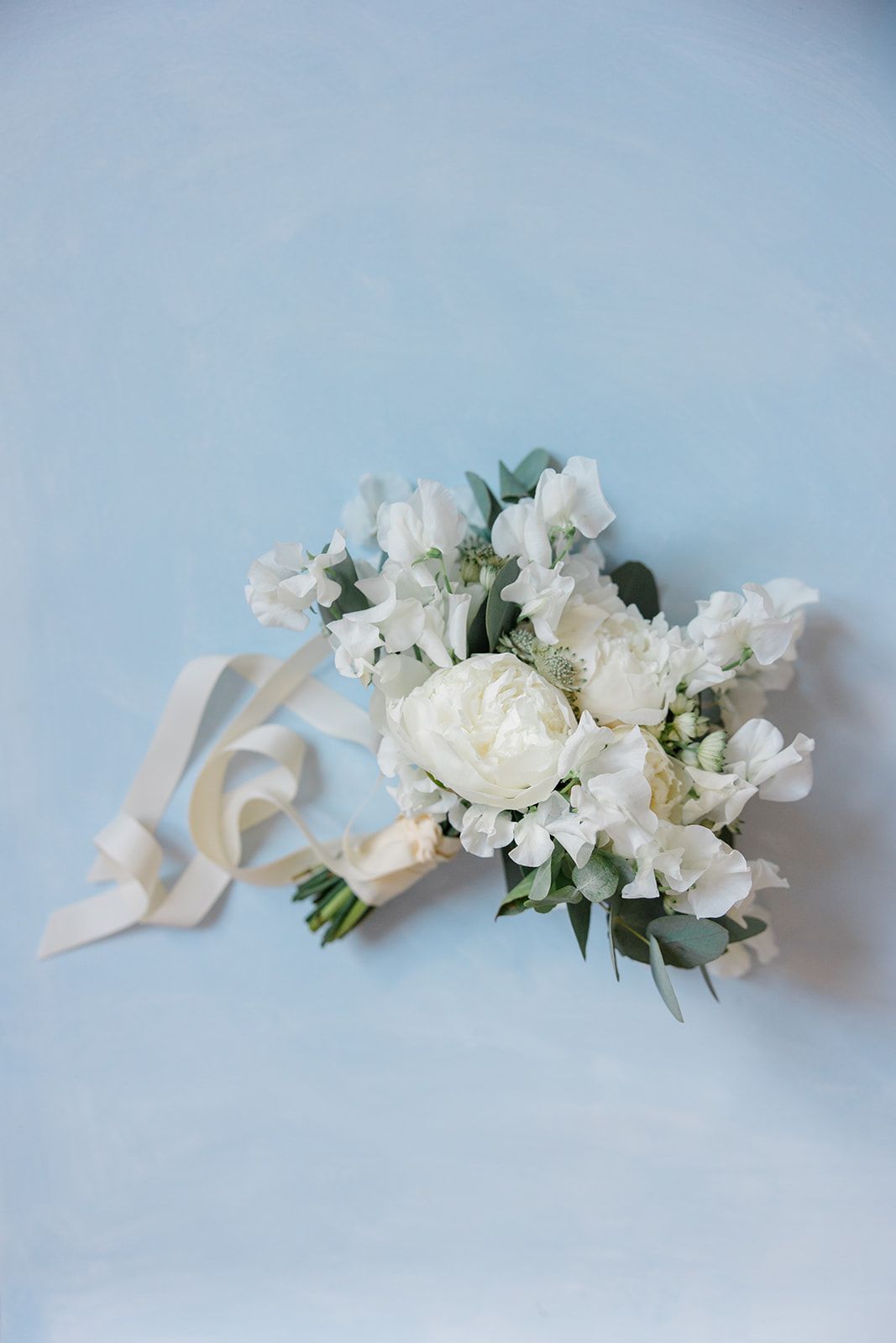 White paper origami crane and delicate floral arrangement on light blue background create an elegant minimalist composition.