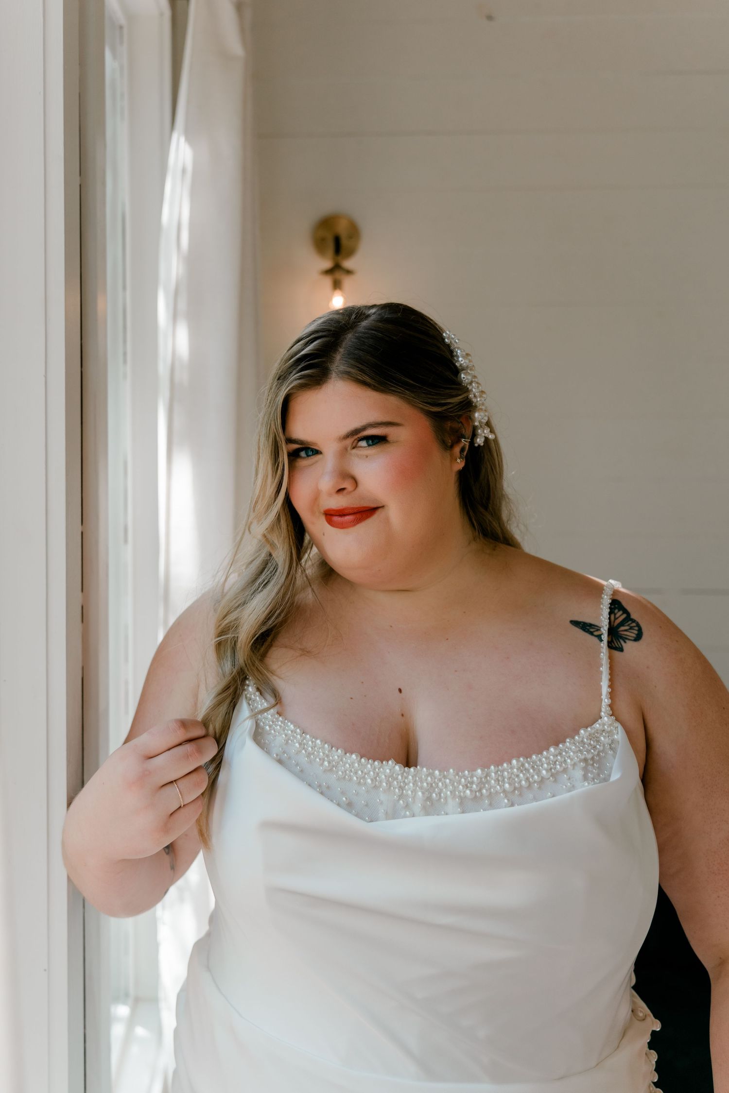 A person wearing a white lace-trimmed slip dress poses against a white wall in soft natural lighting.