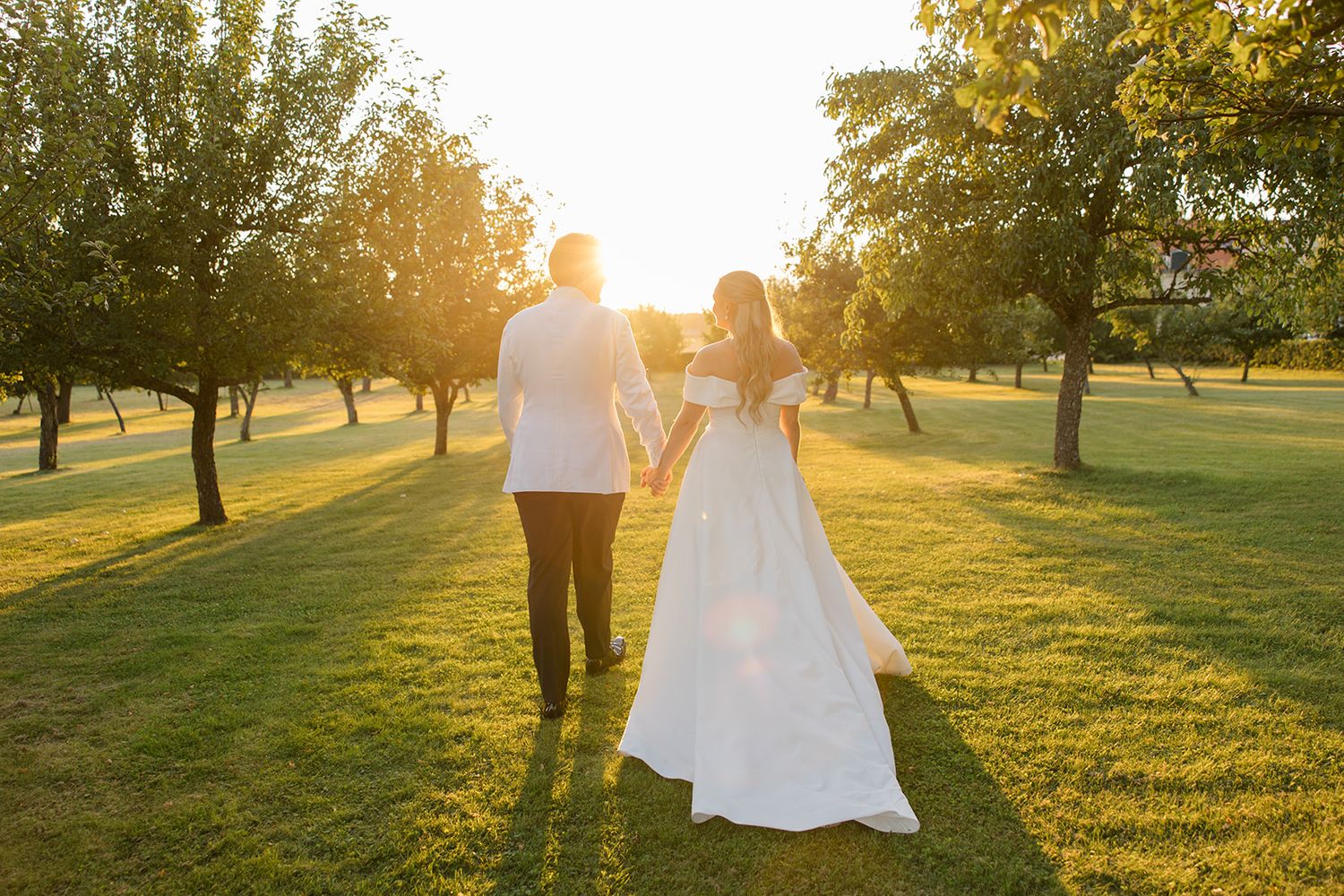 A couple walks through a sunlit park at golden hour with long shadows cast across the grass.