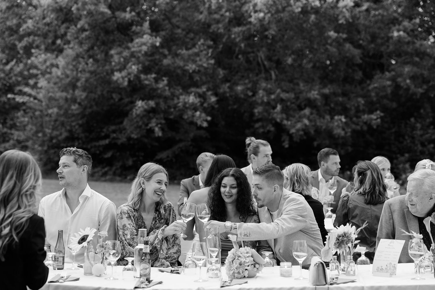 Wedding guests enjoy conversation and drinks at outdoor reception tables during golden hour.