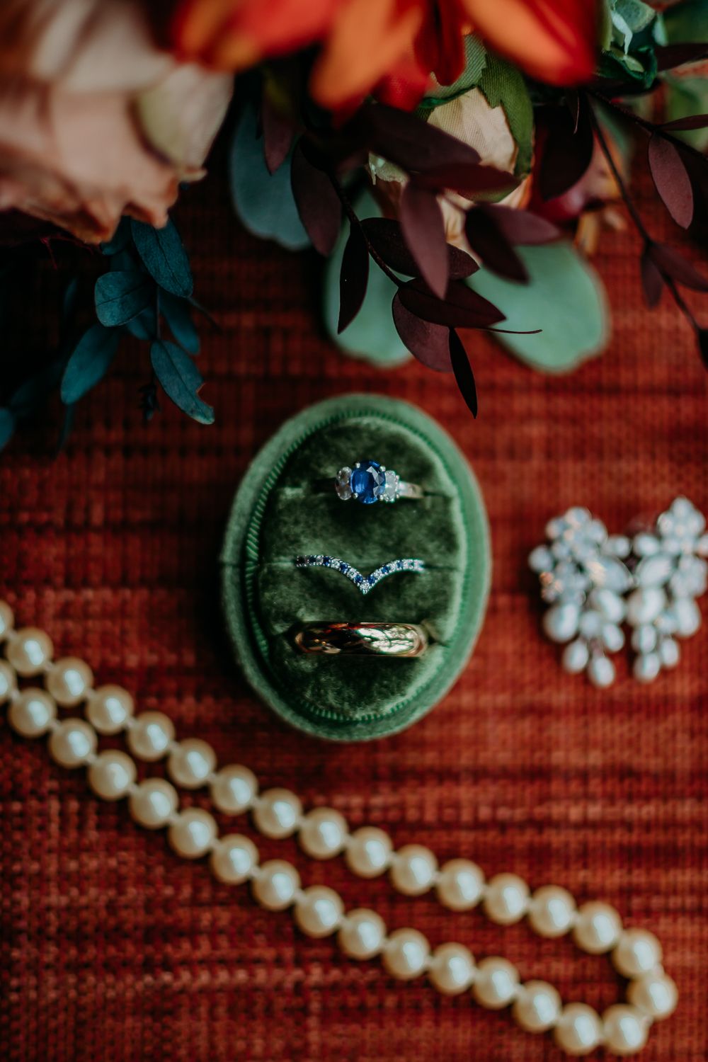 Engagement ring and pearl necklace styled with green velvet ring box and floral accents.