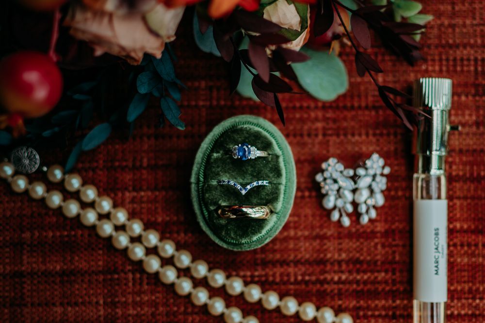 Wedding jewelry and accessories arranged with pearl necklace on red textured background.