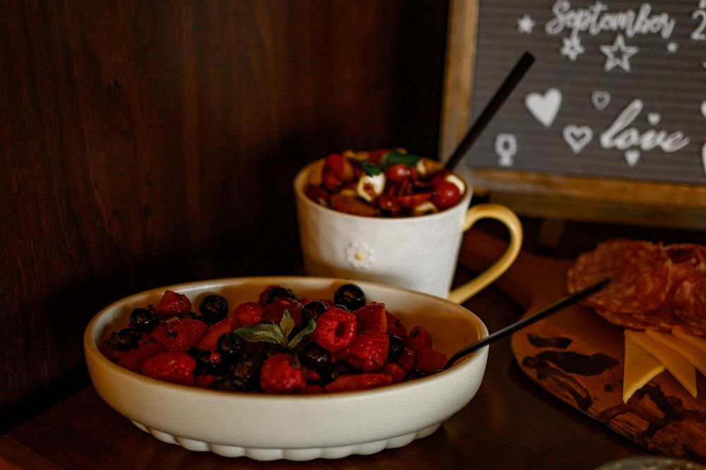 Rustic wooden table with fresh berries, honey, and snacks arranged in a cozy setting.
