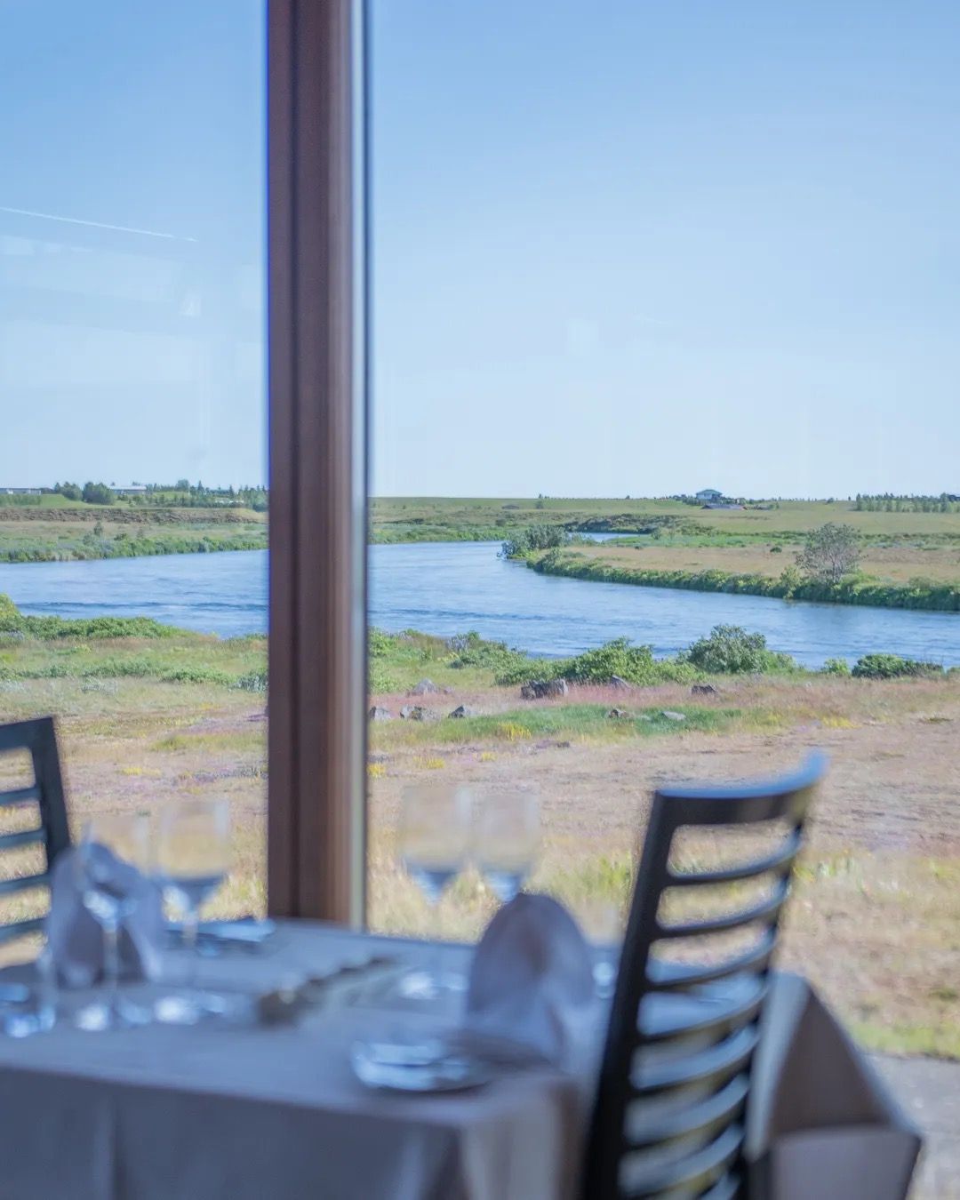 Restaurant table set near a window overlooking a peaceful lagoon and open landscape.