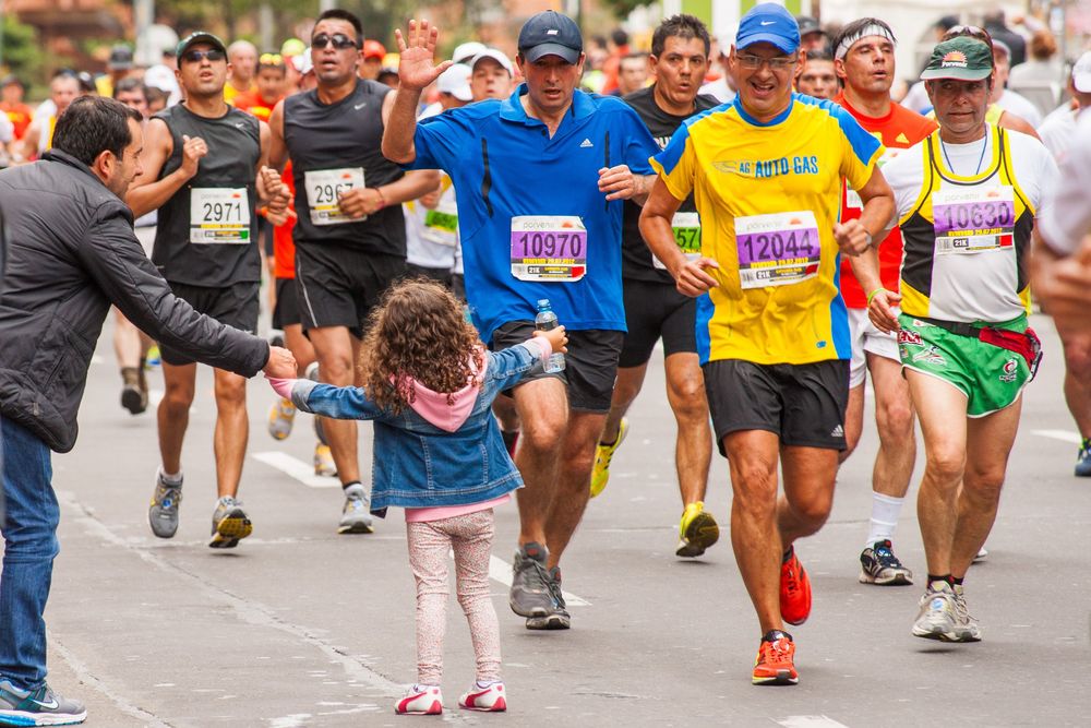 A young child high-fives marathon runners during a road race as spectators and participants crowd the street.