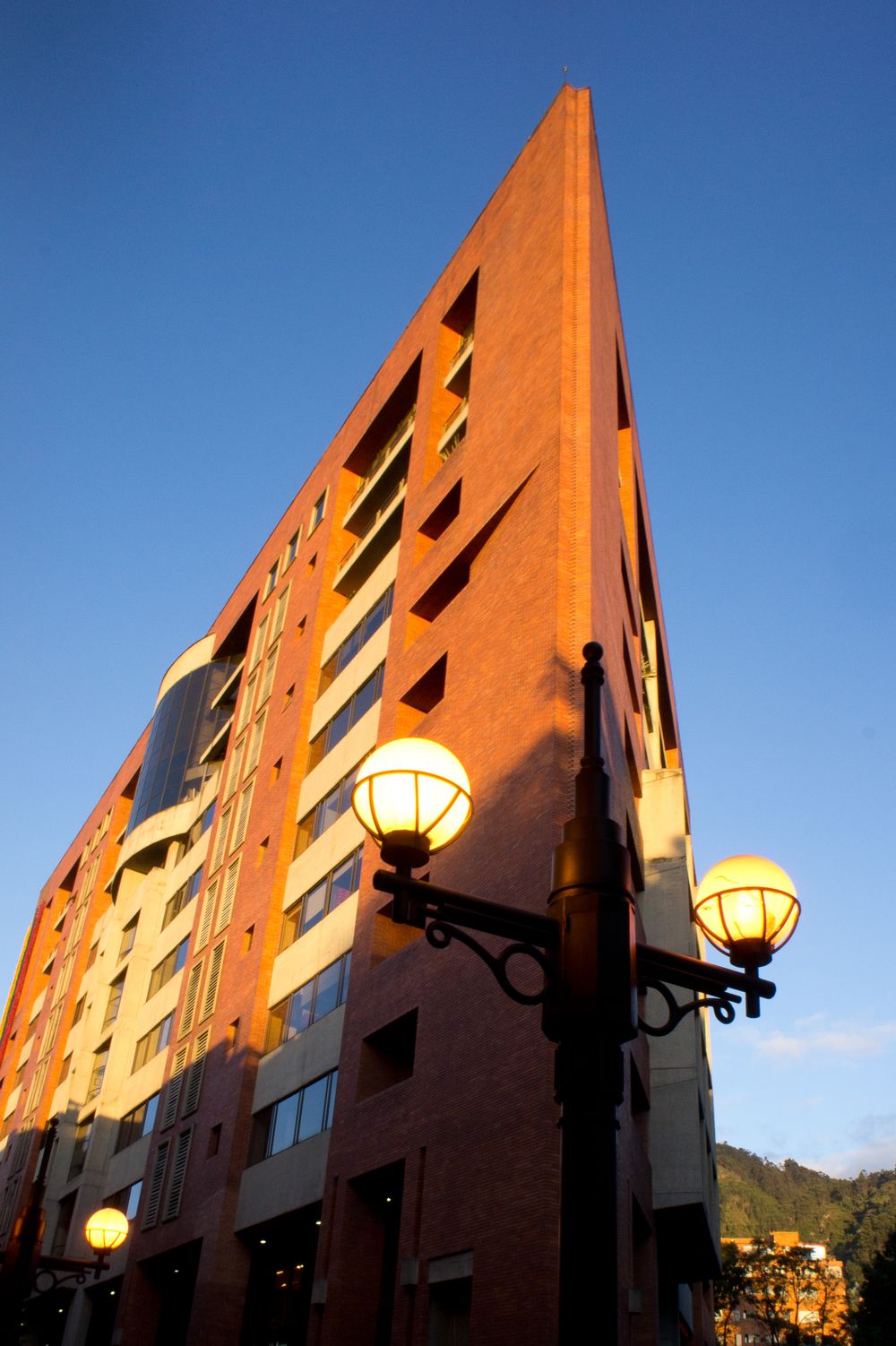 Modern orange building facade photographed from below against bright blue sky with decorative street lamps.