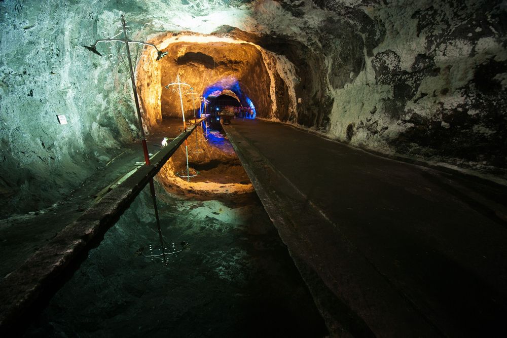 Underground tunnel in an abandoned mine with dark rough walls and dim lighting extending into the darkness.