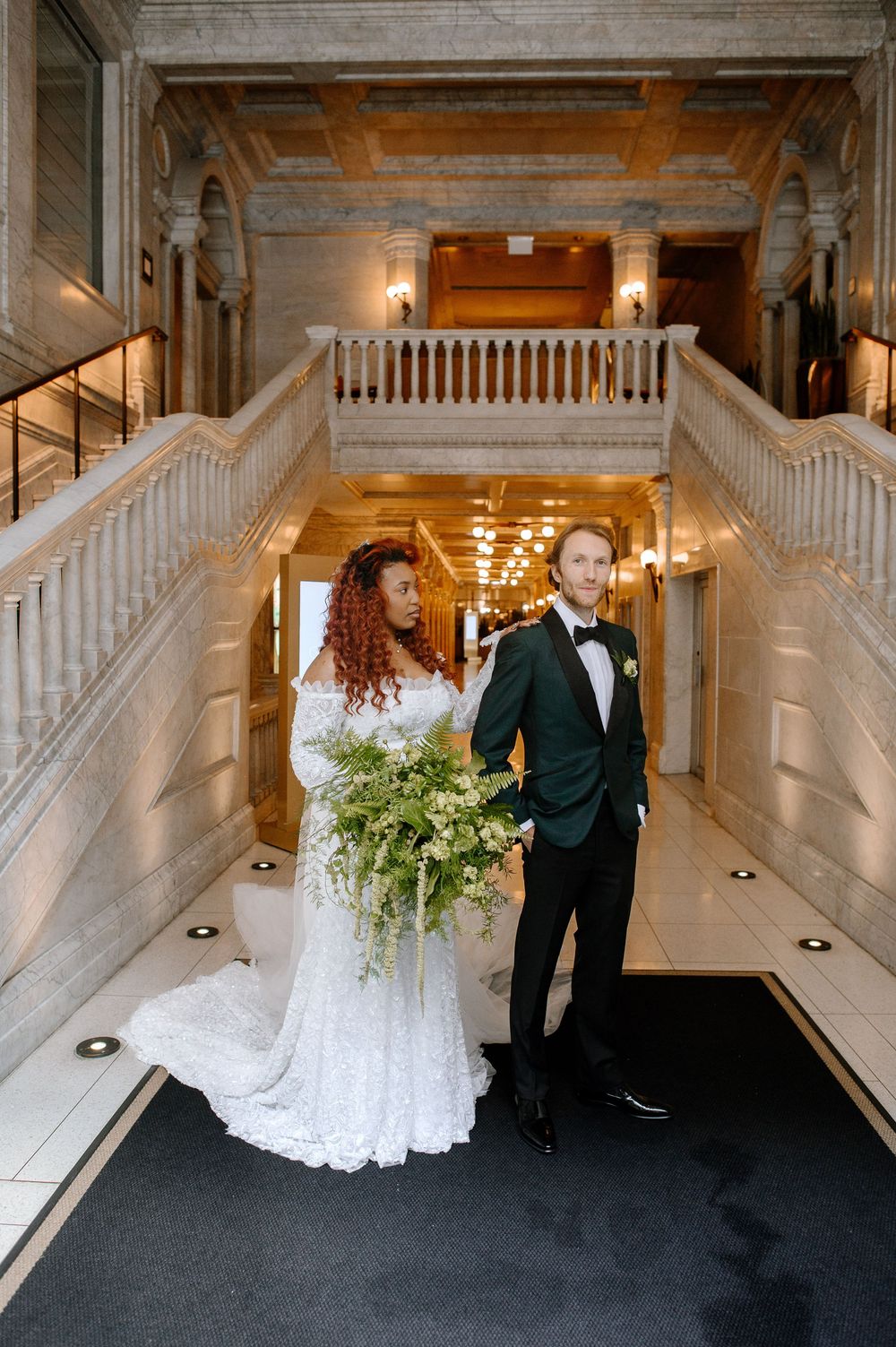 Elegant wedding couple photographed at different angles on grand staircase in luxurious venue with white marble decor.