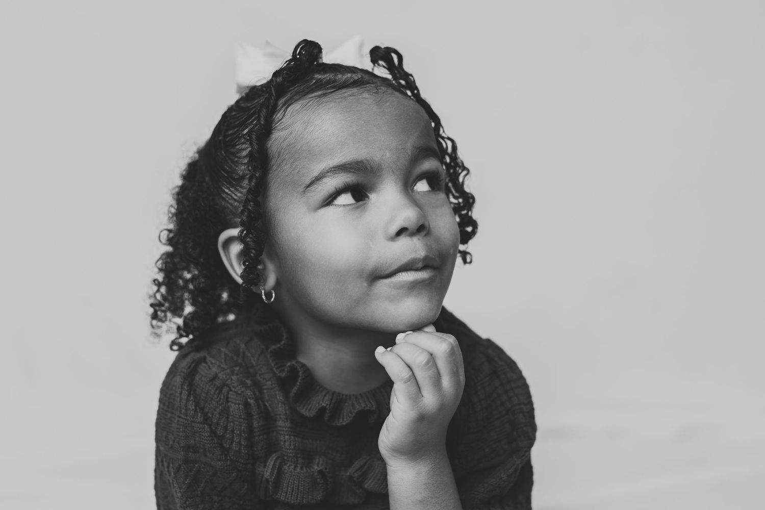 Black and white portrait of a child with curly hair in a dark sweater looking thoughtfully upward.