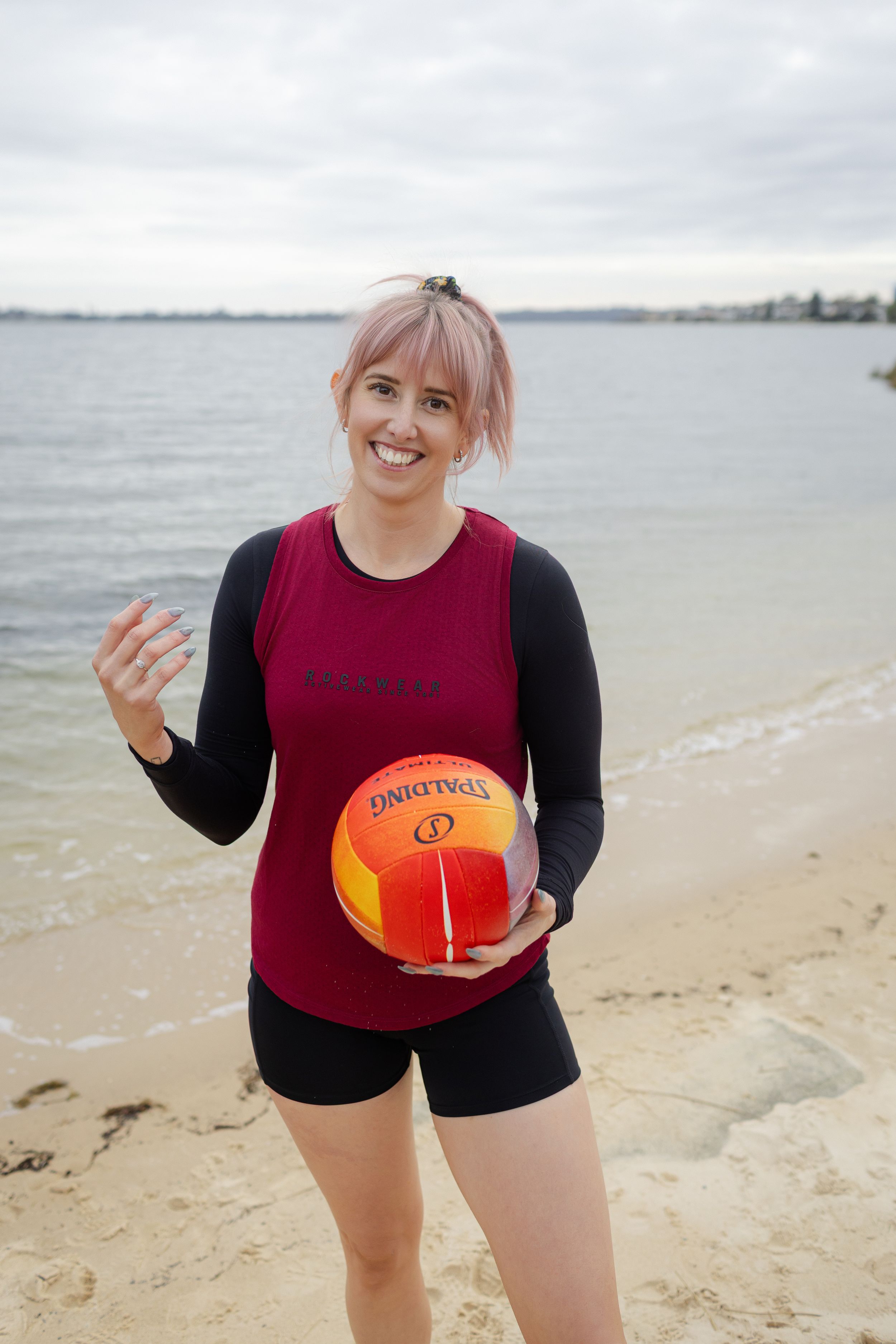 Someone wearing black and burgundy activewear holds an orange ball while playing and having fun at the beach.