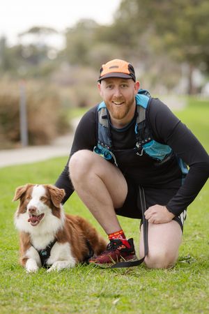 Person in black clothing playing and posing with a brown and white dog on green grass outdoors.