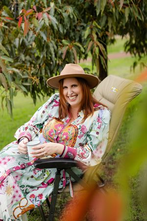 A relaxed scene showing someone enjoying a drink in a floral dress and tan hat while lounging in an outdoor chair.