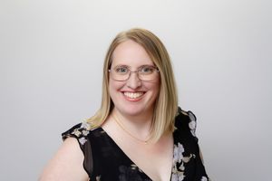 Professional headshot against gray backdrop showing person in black and white patterned dress.