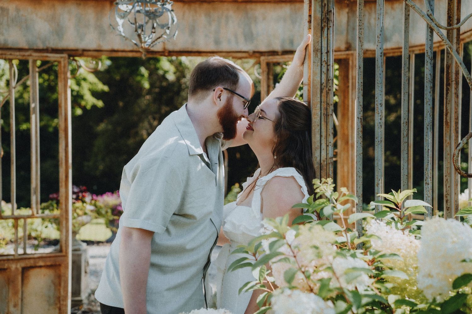 A romantic moment between a couple in a rustic greenhouse garden setting with lush greenery and flowers.