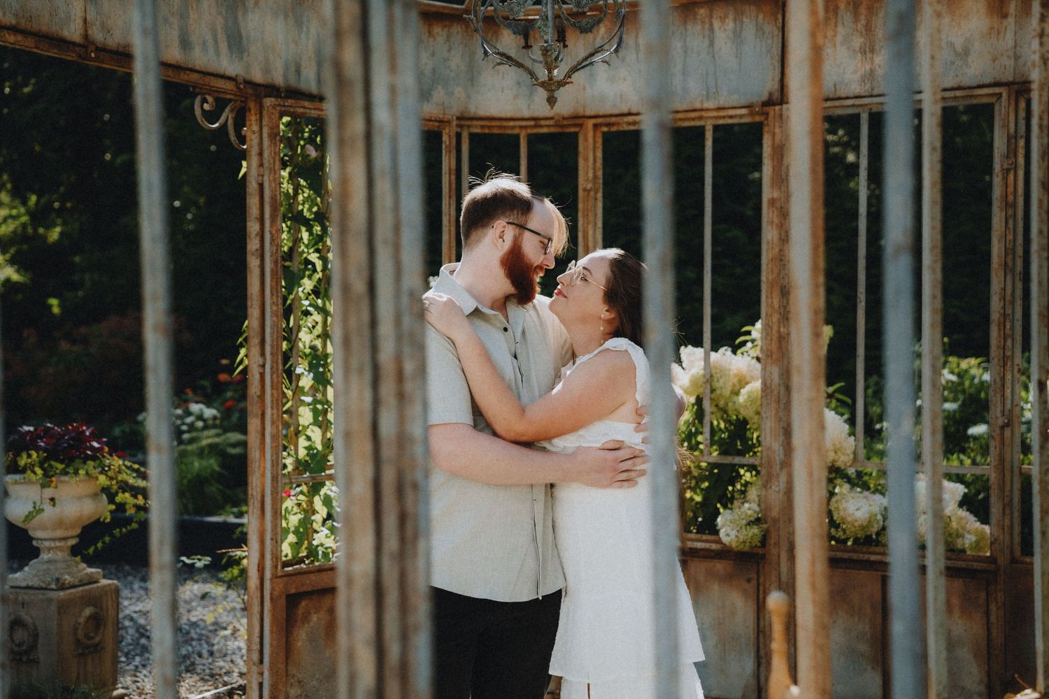 Intimate embrace between a couple in an antique greenhouse with natural light streaming through windows.