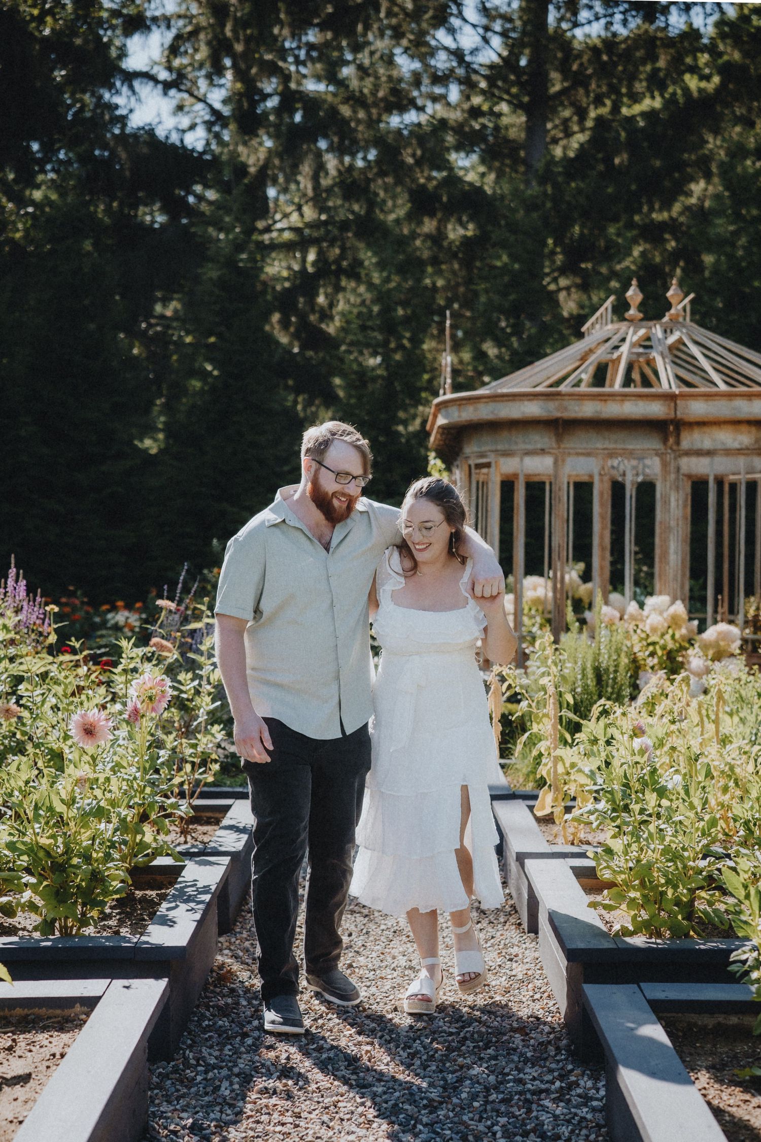 Couple walking together through a garden path with a decorative gazebo in the background.