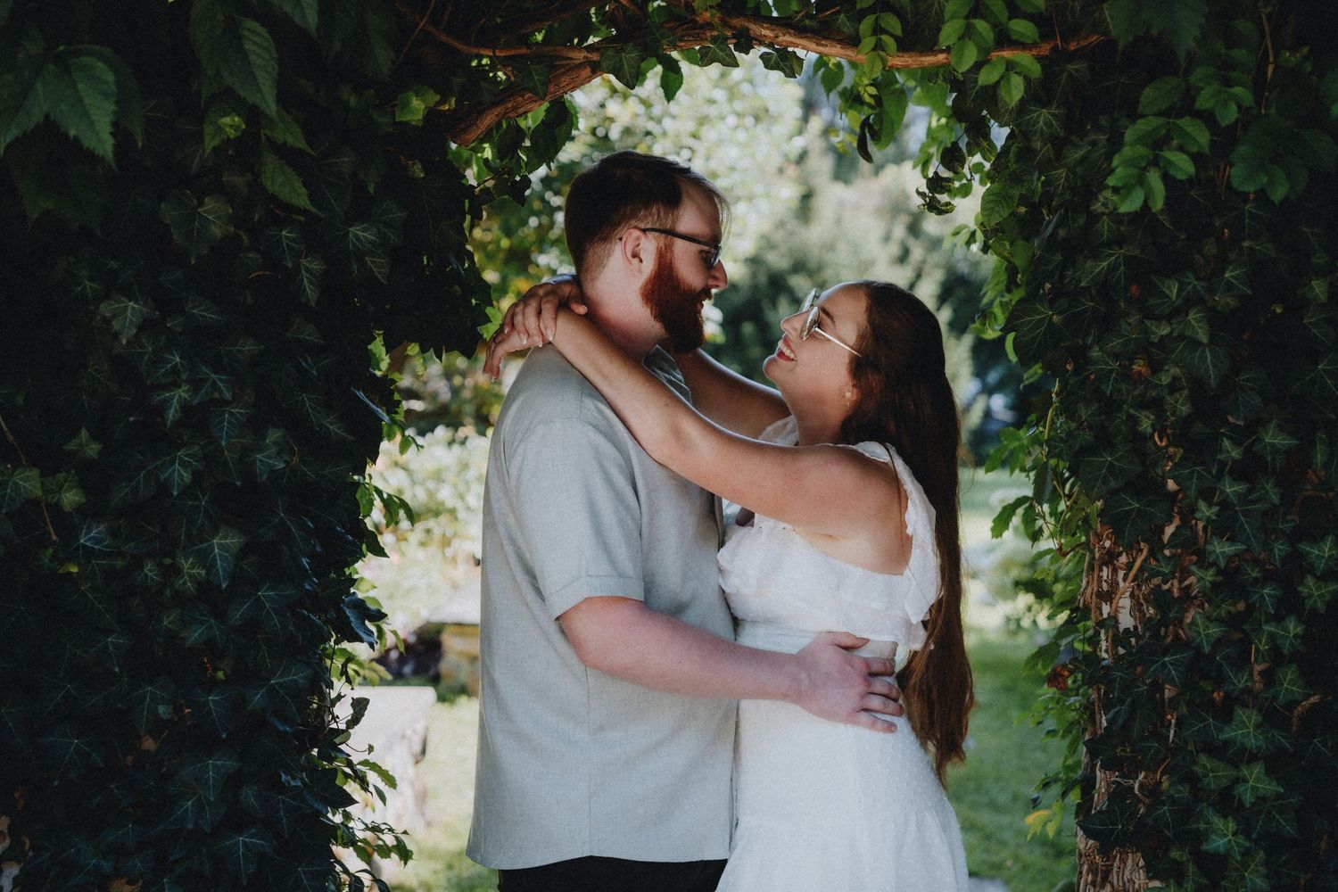 Intimate embrace under a lush green garden archway with natural light filtering through.