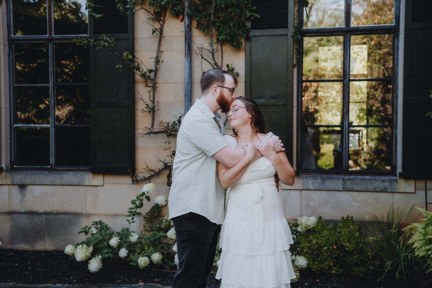 Romantic moment shared between a couple against a vine-covered building exterior.