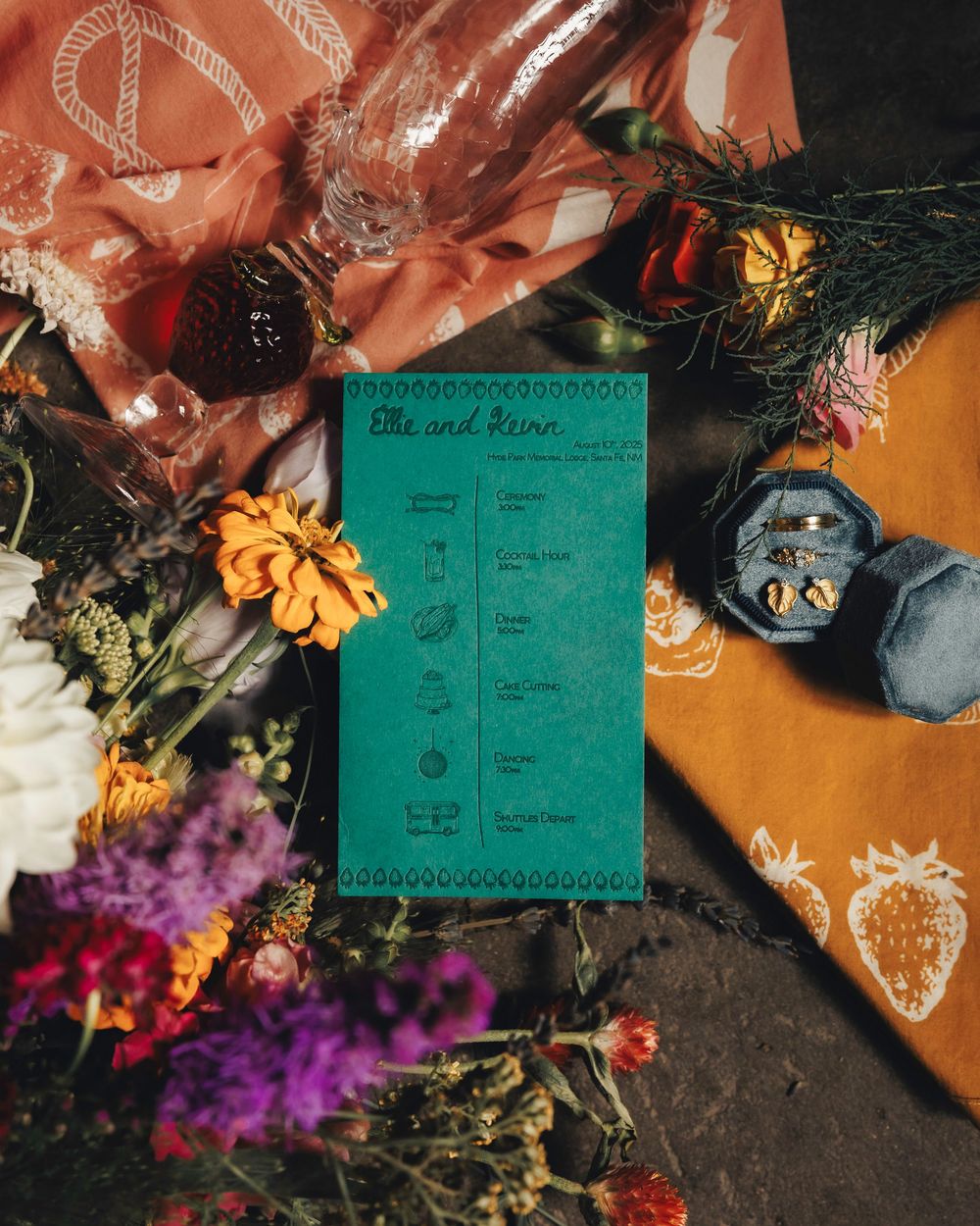 Teal wedding program for Ellie and Kevin surrounded by colorful wildflowers and rings.