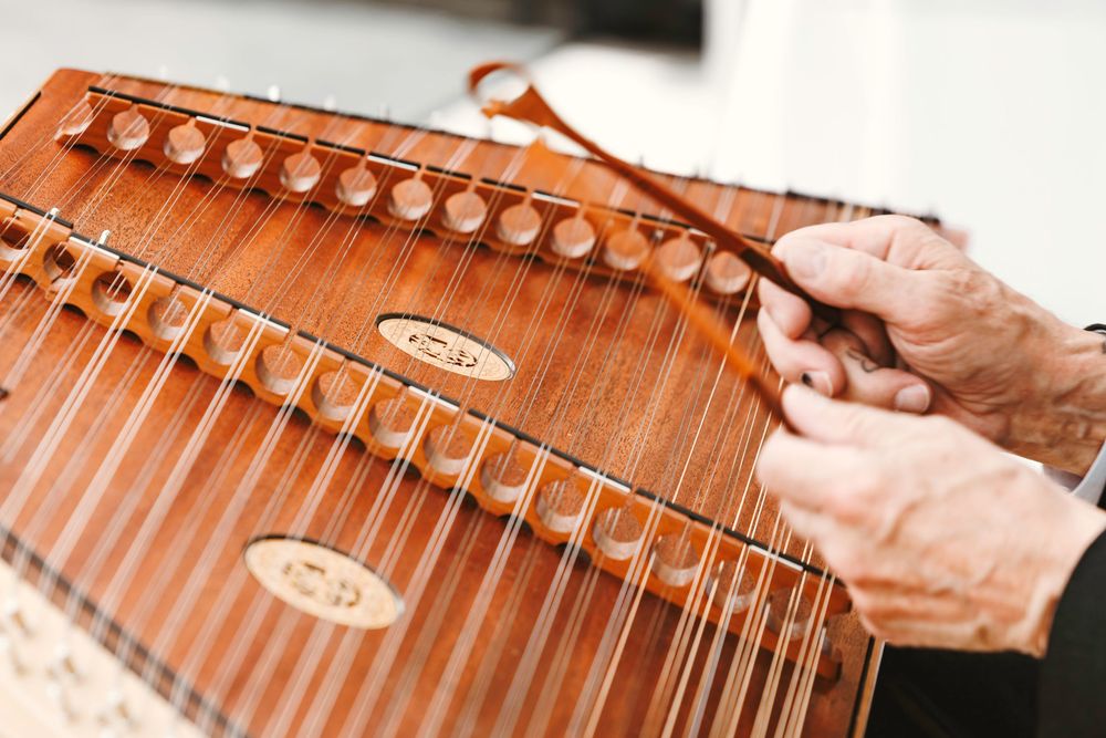 Close-up of elderly hands playing a traditional wooden zither string instrument at a wedding celebration.