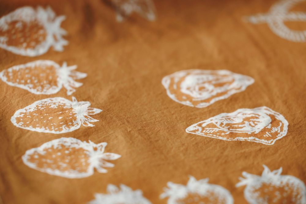 Close-up of golden mustard linen fabric printed with white strawberry and shell botanical illustrations for wedding decor.