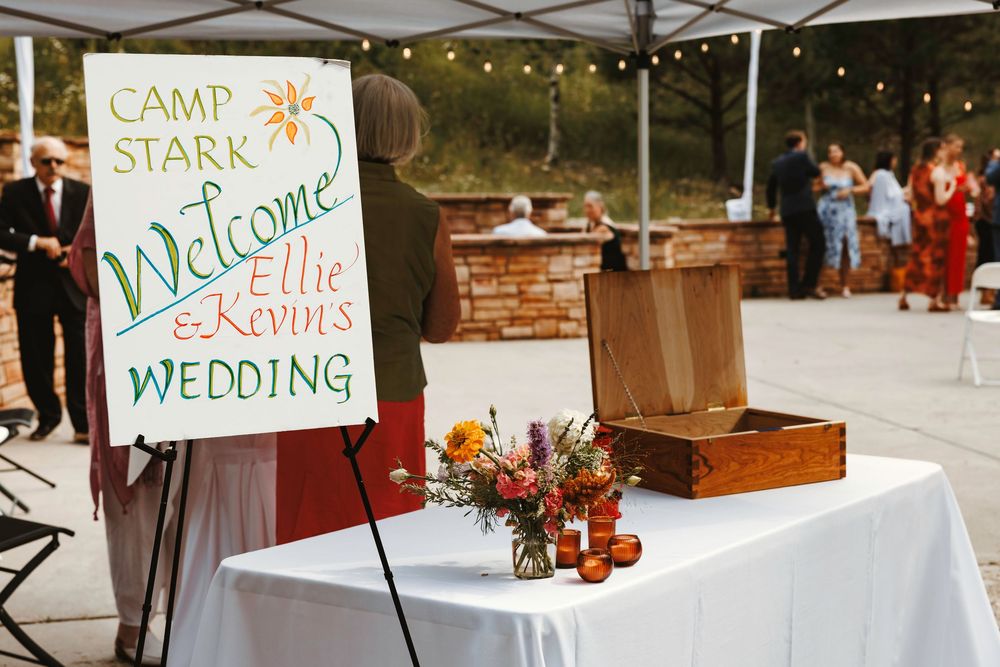 Camp Stark welcome sign for Ellie and Kevin's wedding with colorful flowers on a table.