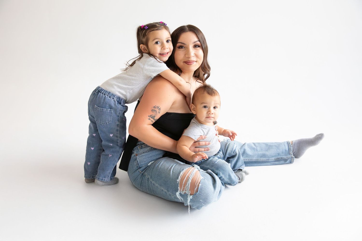 A family in casual denim sits together on a white backdrop for a minimalist portrait session.