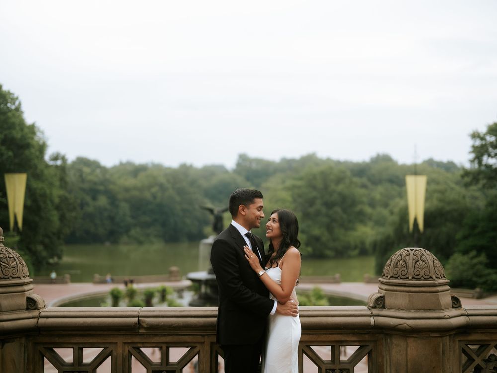 A couple embraces on a stone balcony overlooking a misty landscape during golden hour.