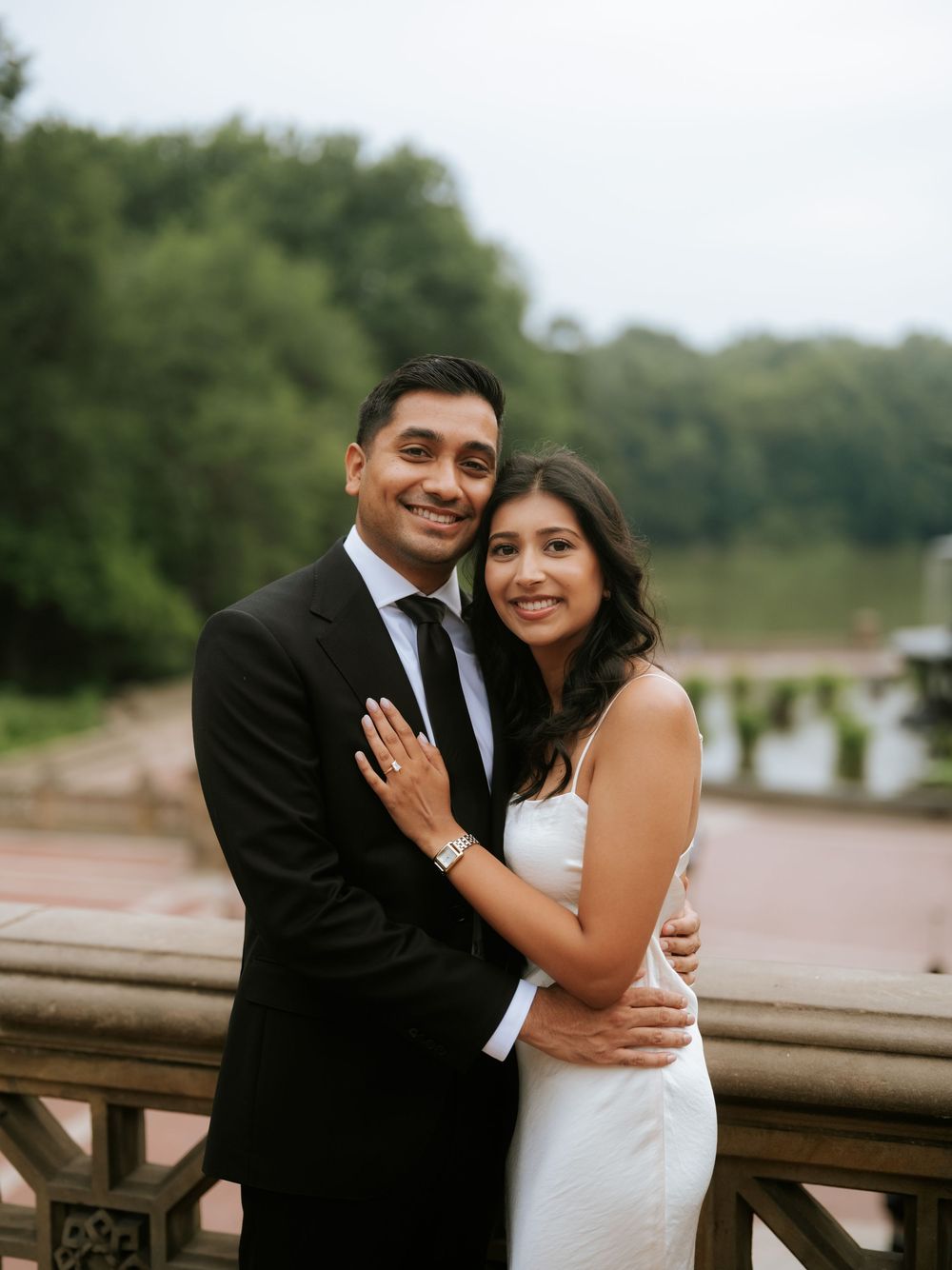 Couple in formal attire embraces near a railing during sunset photoshoot.