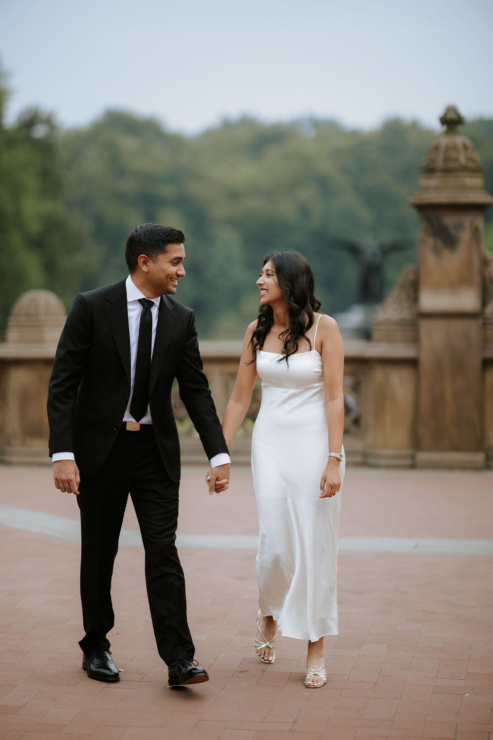 A couple walks playfully along Bethesda Terrace in Central Park wearing formal attire.