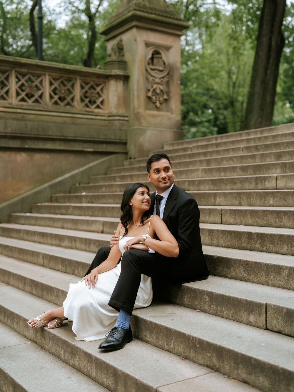 A couple shares playful and candid moments while lounging on historic stone steps in a park.